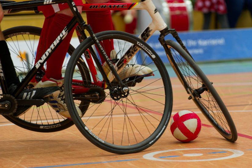 Foto zweier Radballräder, während des Kampfes um den Ball, wobei der Fokus auf die Vorderräder und den Ball gelegt ist.