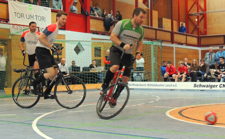 Ein Radballspiel, wobei zwei Spieler dem Ball hinterherfahren.